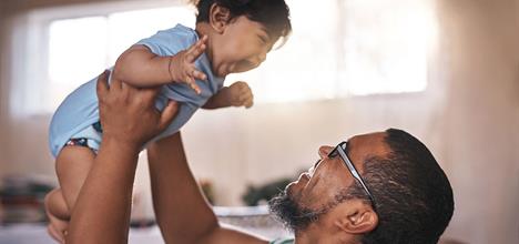 man holds up baby daughter and they laugh
